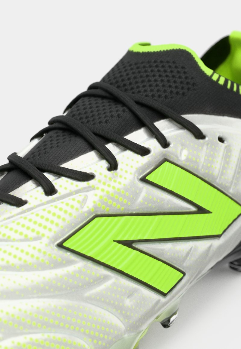 Primo piano di un scarpino da calcio argento e verde neon con lacci neri e upper in rete.