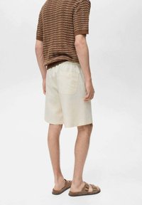 Beige, knielange shorts van een lichte stof met een elastische tailleband en een achterzak. Draagt een bruin, gestreept kortmouwenshirt.