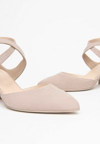Nude suede low-heeled shoes with a pointed toe and crisscross ankle straps. Smooth texture, minimalistic design, and structured silhouette.