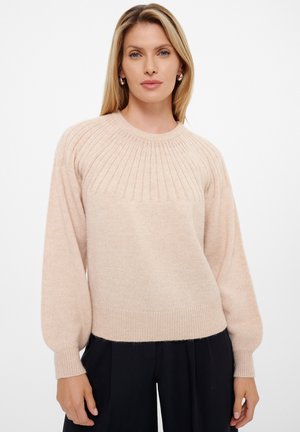 Pull en maille rose clair avec texture côtelée, encolure ronde et manches ballon, associé à un pantalon large noir.