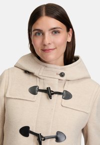 Beige gyapjú duffle kabát kapucnival, fekete gombokkal és texturált felületű zsebekkel. Figyelj a kontrasztos részletekre és varrásokra.