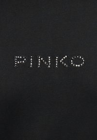 Μαύρο ύφασμα με τη λέξη "PINKO" σχηματισμένη από μικρές, ομοιόμορφα τοποθετημένες ασημένιες καρφίτσες που σχηματίζουν κάθε γράμμα.
