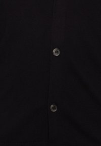 Svart cardigan i stickad tyg, med två runda, svarta knappar fram. Texturen är något ribbad och slät.