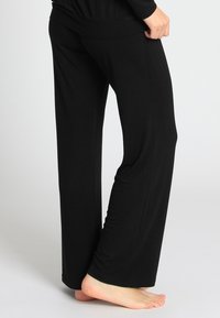 Schwarze, fließende Hosen aus einem weichen Stoff, mit einer lockeren Passform, weitem Bein und hohem Bund, geeignet für die Freizeit.