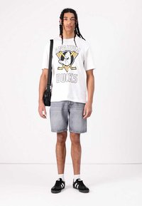 T-shirt blanche avec un graphisme "Anaheim Ducks", short en denim gris et baskets noires avec des accents blancs. Sac crossbody noir.