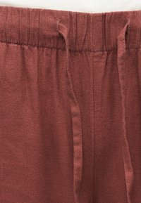 Κοντινό πλάνο παντελονιού σε σκουρόχρωμο σκουριασμένο ύφασμα με ελαστική μέση και κορδόνια που δένουν στο ίδιο χρώμα.