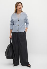 Cardigan en maille bleu clair avec un col en V, cinq boutons et des poignets côtelés, associé à un pantalon large noir et un sac fourre-tout noir.