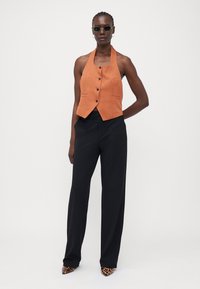 Oransje halterneck vest med en tettsittende design, med en dobbelspent front og to sidelommer, kombinert med svarte, vidde ben bukser.