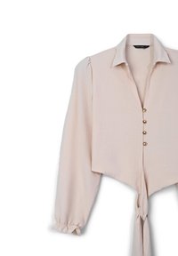 Chemisier rose blush court avec de longues manches bouffantes, fermeture à boutons sur le devant, et détail à nouer au bas. Tissu lisse avec un léger éclat.