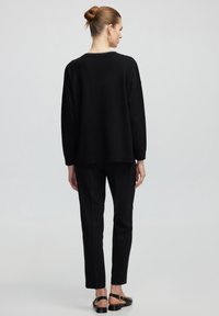 Pull noir surdimensionné avec des manches longues, encolure ras du cou, et pantalon noir à coupe droite. Tissu doux avec une texture mate et un design minimaliste.