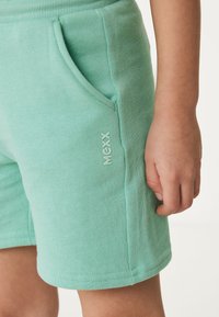Mátově zelené bavlněné šortky s elastickým pasem, bočními kapsami a malým logem na levé straně. Měkká struktura a jednoduchý design.