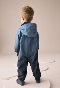 Mėlynas ir tamsiai mėlynas vaikų neperšlampamas kombinezonas su gobtuvu, elastinėmis rankogaliais ir lygiu paviršiumi, skirtas naudoti lauke.