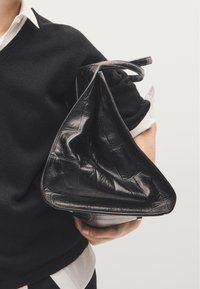 Borsa in pelle nera con forma triangolare, caratterizzata da un motivo texturizzato a coccodrillo, bordi morbidi e un manico singolo per il trasporto.