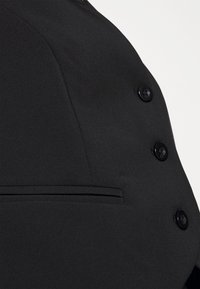 Schwarzer Blazer mit glatter Stoffstruktur, doppelt geknöpftem Design, sechs runden Knöpfen und einer seitlichen Tasche.
