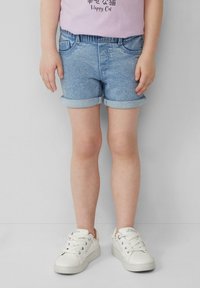 Lichtblauwe denimshorts met opgerolde cuffs, voorzien van twee voorzakken en een gladde textuur. Gecombineerd met witte sneakers.