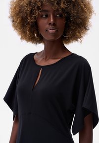 Schwarzes Kleid mit kurzen, weiten Ärmeln und Ausschnittdetail an der Halslinie. Hergestellt aus weichem, glattem Stoff mit tailliertem Oberteil.