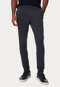 Cino grigio scuro in una vestibilità slim, con una texture liscia e tasche laterali, abbinati a sneakers nere con suole bianche.