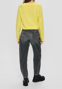 Långärmad randig skjorta i klar gul med ribbat mönster, tillsammans med högmidjade svarta jeans och kraftiga svarta skor.