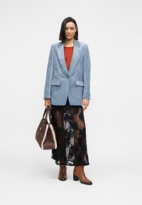 Lichtblauwe corduroy blazer, roestkleurige top, zwarte maxirok van kant, bruine leren enkellaarzen, en een bruine tas met schapenvachtdetail.