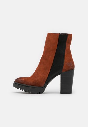 Bottine femme à talon bloc, devant en suède rouille, panneau arrière en suède noir, semelle à crampons et logo papillon discret près du talon.