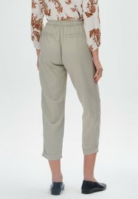 Jasnoszare, krótkie spodnie o luźnym kroju, z elastycznym pasem i dwoma tylnymi kieszeniami, w połączeniu z wzorzystą bluzką z długim rękawem.