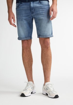 Shorts en denim bleu clair avec revers roulés, présentant une coupe classique et cinq poches. Associés à des baskets blanches avec des accents noirs.