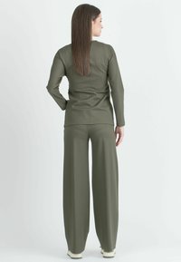 Olivgrünes Zweiteiler-Outfit mit einem Langarmoberteil und weit geschnittenen Hosen, gefertigt aus einem glatten, elastischen Stoff und mit einer lockeren Passform.