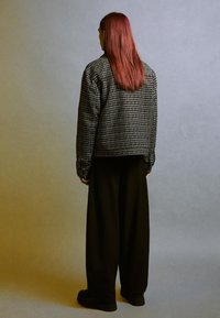 Czarna i biała kratkowana kurtka z długimi rękawami, połączona z czarnymi spodniami o szerokich nogawkach i czarnymi butami, widok z tyłu.