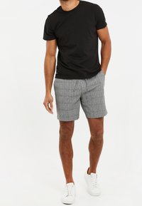Camiseta de algodón negra, pantalones cortos de cuadros grises y zapatillas deportivas blancas. Los pantalones cortos tienen una cintura elástica y bolsillos laterales.