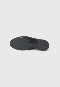 Zwarte rubberen schoenen zool met een gladde afwerking, ronde vorm en getextureerde rand. Bevat een reliëflogo ontwerp en een ondiep profiel.