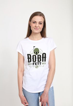 T-shirt en coton blanc avec un design graphique en texte noir et vert portant l'inscription "BOBA FETT Chasseur de Primes", accompagné d'une illustration de casque.