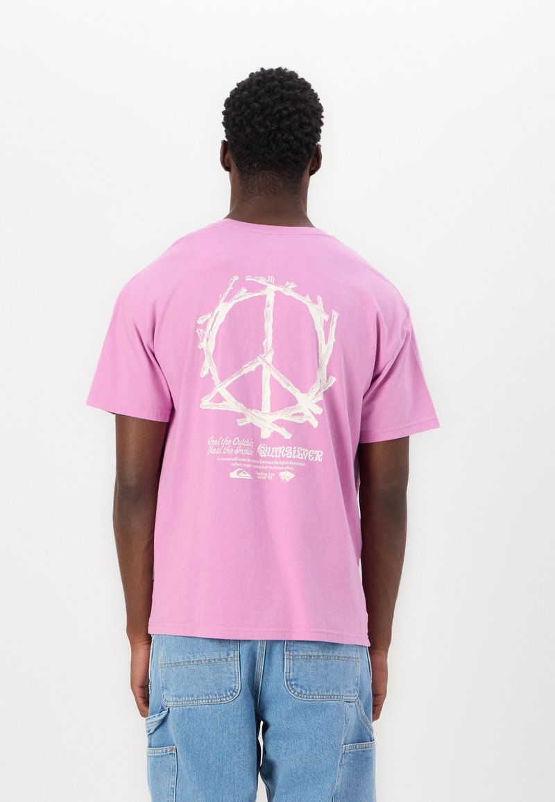 T-shirt en coton rose avec un grand graphique de symbole de paix blanc au dos, accompagné d'un texte dans une police plus petite sous le design.