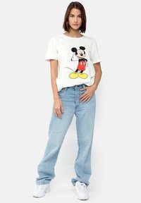 Hvid bomulds t-shirt med et sort og rødt Mickey Mouse grafik. Kombineret med lyseblå, løstsiddende jeans og hvide sneakers.