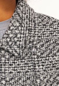 Šedý a černý texturovaný límec s tkaným vzorem. Tkanina vypadá nadýchaně a obsahuje různé tloušťky nití, což zvyšuje vizuální hloubku.