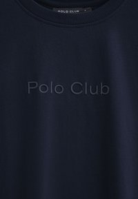 Marinblå sweatshirt med upphöjd text "Polo Club" på bröstet och ribbad halslinning.