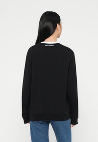 Sort sweatshirt med lange ærmer, ribbede manchetter og en hvid krave. Har "KARL LAGERFELD" logo på den bagerste halsudskæring. Klassisk pasform.