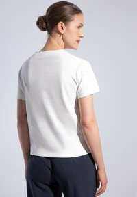 T-shirt bianco a maniche corte con scollatura rotonda, texture liscia e vista posteriore che mostra una leggera sartoria. Abbinato a pantaloni blu navy.