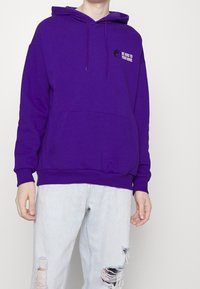Sudadera de algodón morada con bolsillo canguro, capucha con cordón y el texto "SE AMABLE CON TU MENTE" junto a un símbolo de yin-yang en el pecho.