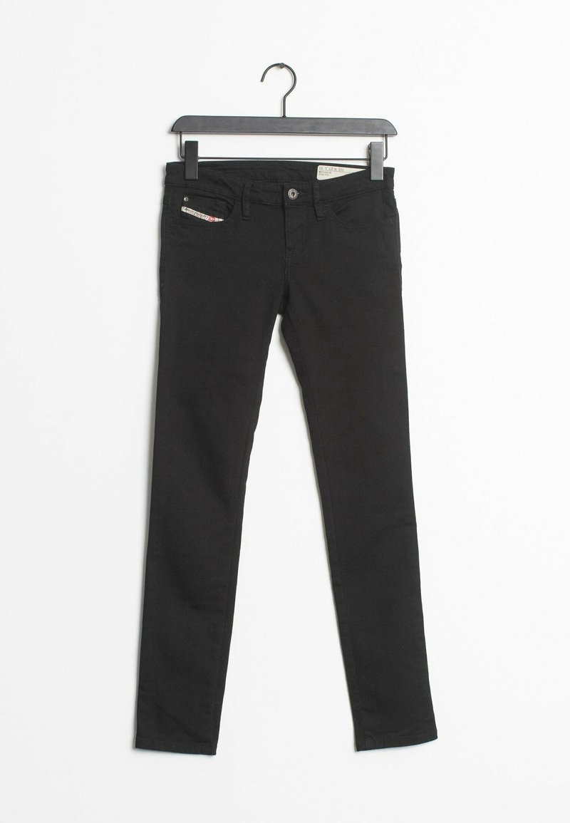 Jean skinny noir avec une texture lisse, comportant une petite poche décorative et une fermeture à bouton en métal. Suspendu à un cintre en plastique noir.