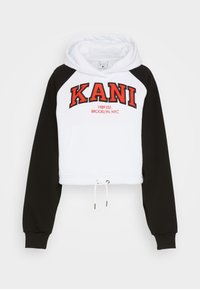 Hanorac scurt cu fața albă și mâneci raglan negre, având textul roșu "KANI" și un șnur la baza lui. Textură de material moale.