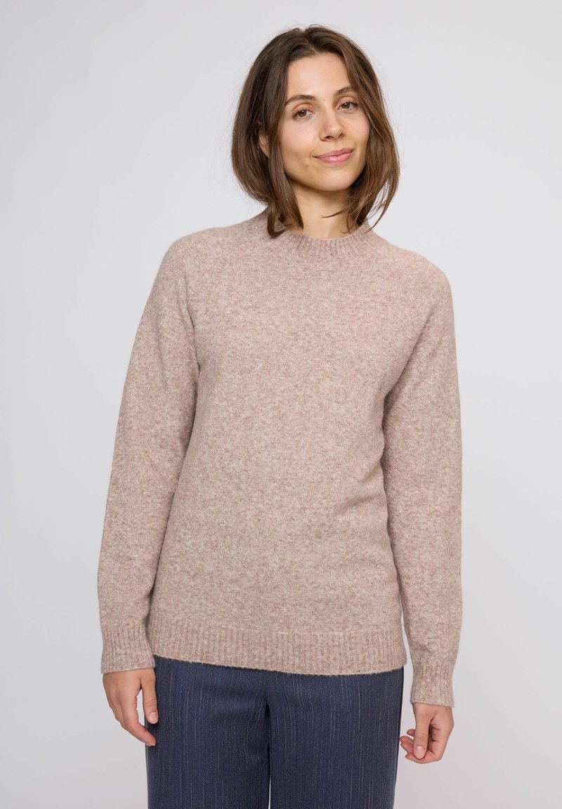 Maglione lavorato a maglia di un delicato colore rosa con scollo a giro e maniche lunghe; presenta una consistenza morbida e polsini e orlo a coste. Indossato con pantaloni a righe blu navy.