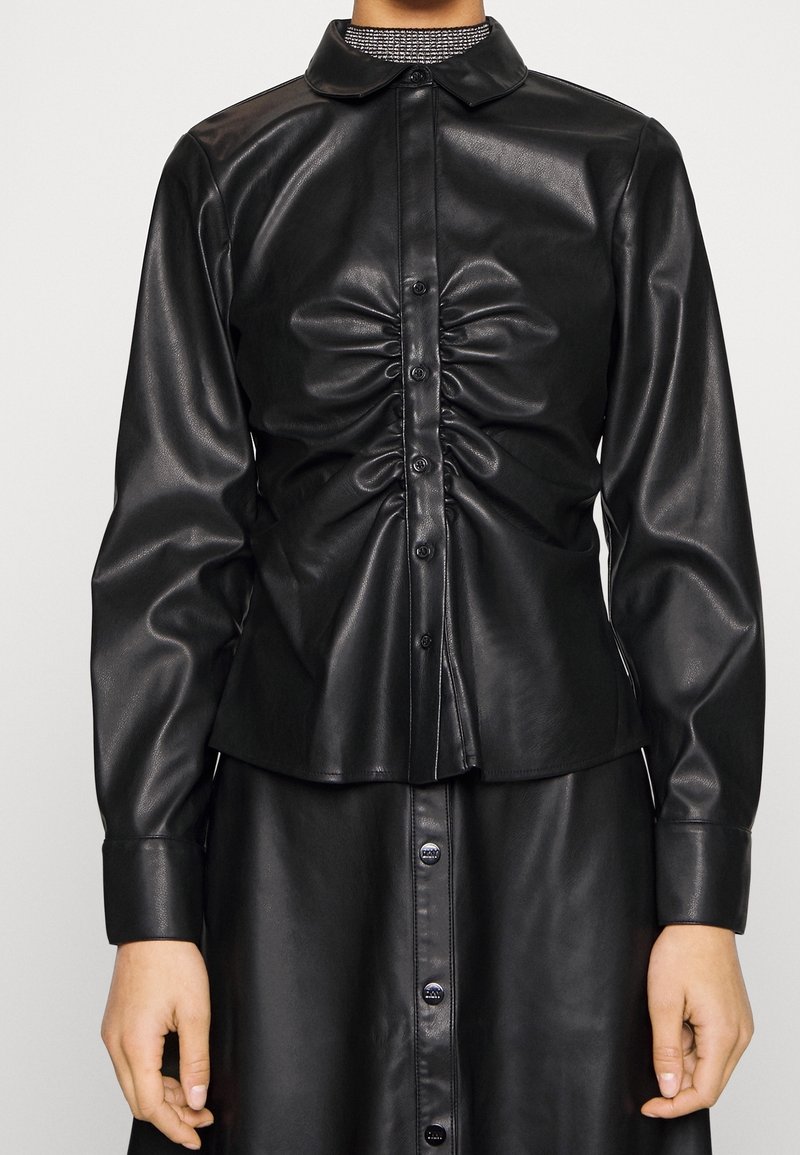 Black leather shirt with a slim fit, featuring a pleated front, button closure, and a rounded collar. Long sleeves with buttoned cuffs.