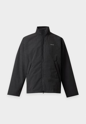 Veste noire zippée avec col haut et poches latérales, avec un petit logo blanc de la marque sur la poitrine, posée à plat sur un fond clair.
