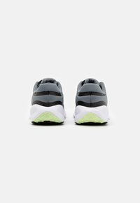 Baskets de sport grises avec des accents noirs et une semelle blanche, présentant une surface texturée et une semelle extérieure traction verte.