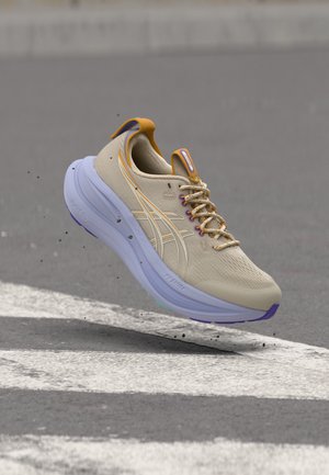 Chaussure de course beige clair et orange avec une semelle blanche épaisse flottant au-dessus d'une route avec des marquages blancs peints et des débris éparpillés.