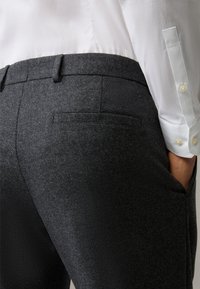 Pantaloni grigi scuri su misura con un tessuto testurizzato, caratterizzati da un frontale piatto, tasche laterali e una singola tasca posteriore.