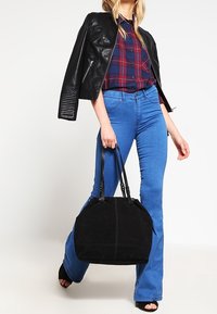 Sac à main en suede noir avec double poignées, forme arrondie et coutures saillantes. Le sac est associé à une veste en cuir noir et un jean évasé bleu.