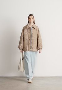 Μπεζ μπουφάν με καπιτονέ, φαρδιά εφαρμογή, μεγάλο γιακά και κλείσιμο με κουμπιά, σε συνδυασμό με ανοιχτό μπλε παντελόνι με φαρδιά πόδια και κρεμ τσάντα ώμου.