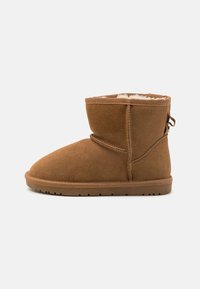 Bottines en suede marron avec un bout arrondi, une doublure intérieure douce et une semelle en caoutchouc flexible. Présentent une couture et une languette à l'arrière.