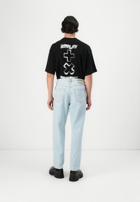 Schwarzes T-Shirt mit weißem grafischem Aufdruck, kombiniert mit hellblauen Jeans und schwarzen klobigen Schuhen. Sichtbare Nähte an den Jeans.